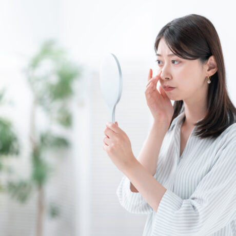 Woman assessing her nose in a mirror before non-surgical rhinoplasty treatment