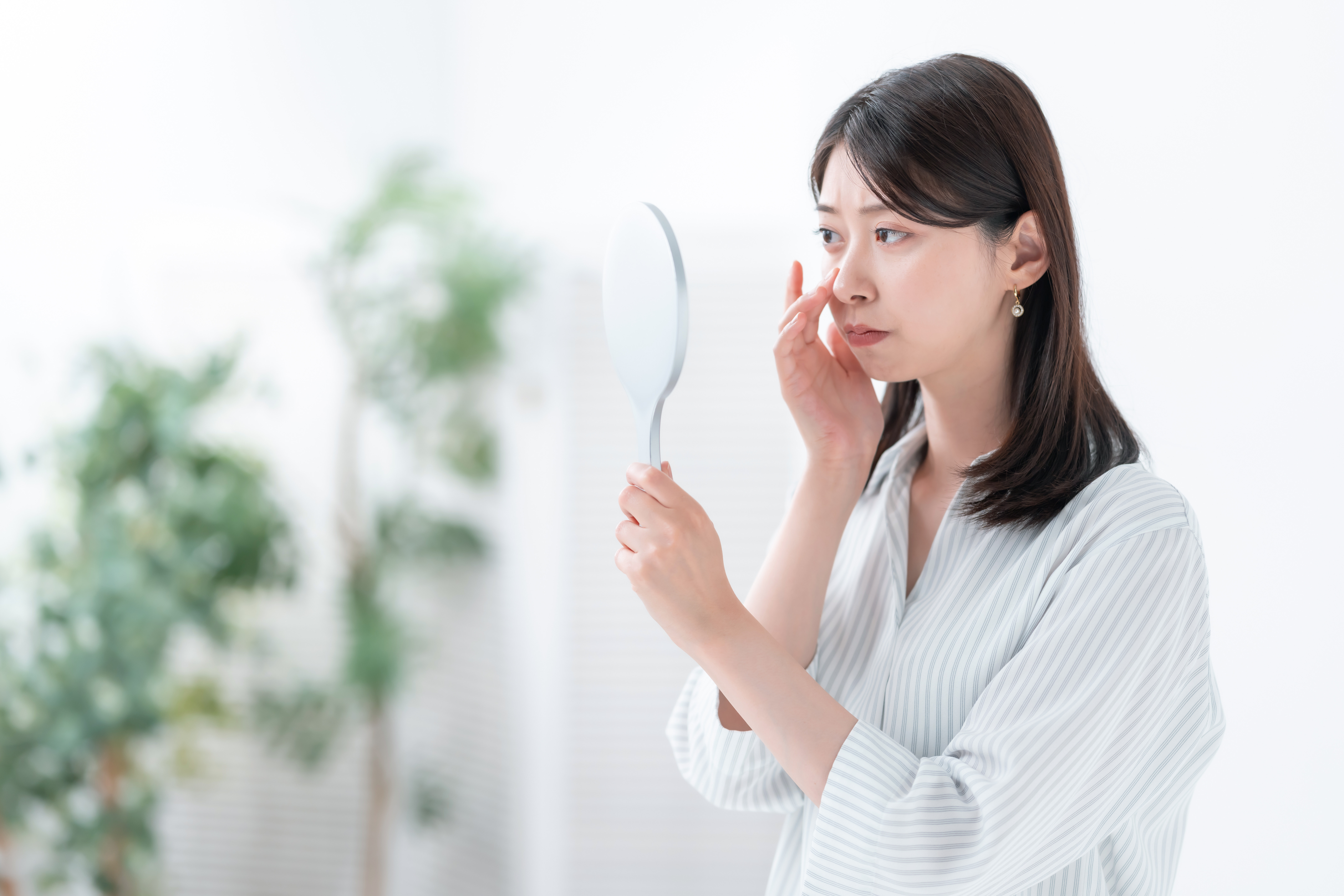 Woman assessing her nose in a mirror before non-surgical rhinoplasty treatment