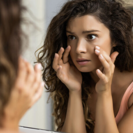 Woman examining under-eye area in mirror showing signs of tear trough hollowing and skin ageing