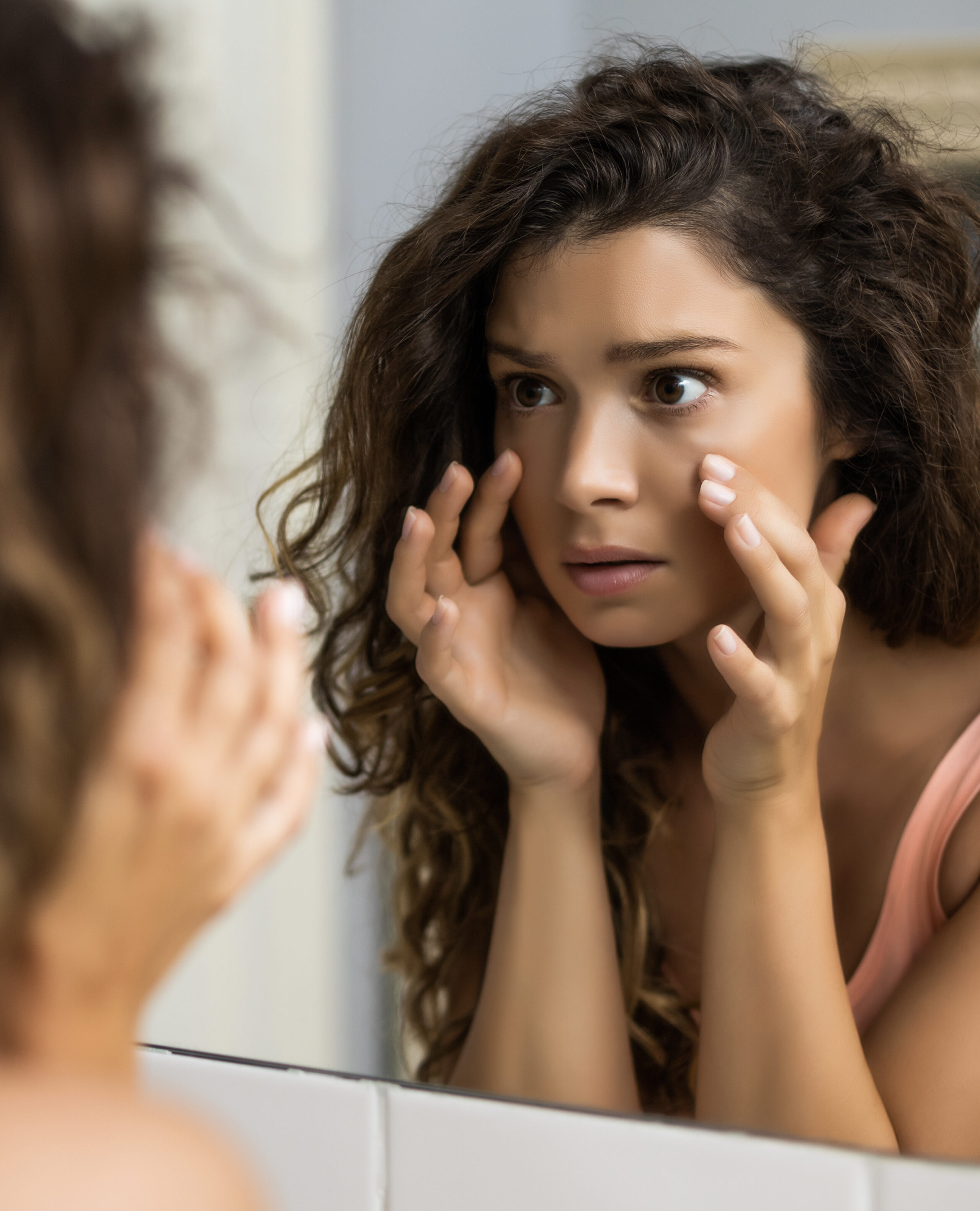 Woman examining under-eye area in mirror showing signs of tear trough hollowing and skin ageing